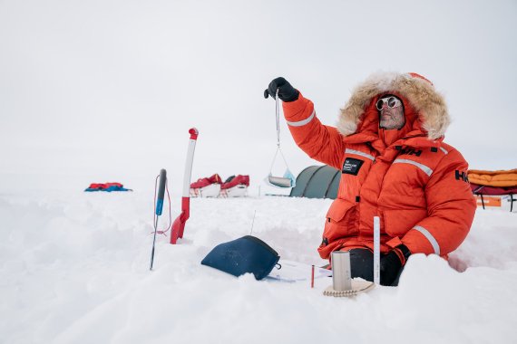 Mann mit orangener Jacke sitzt im Schnee